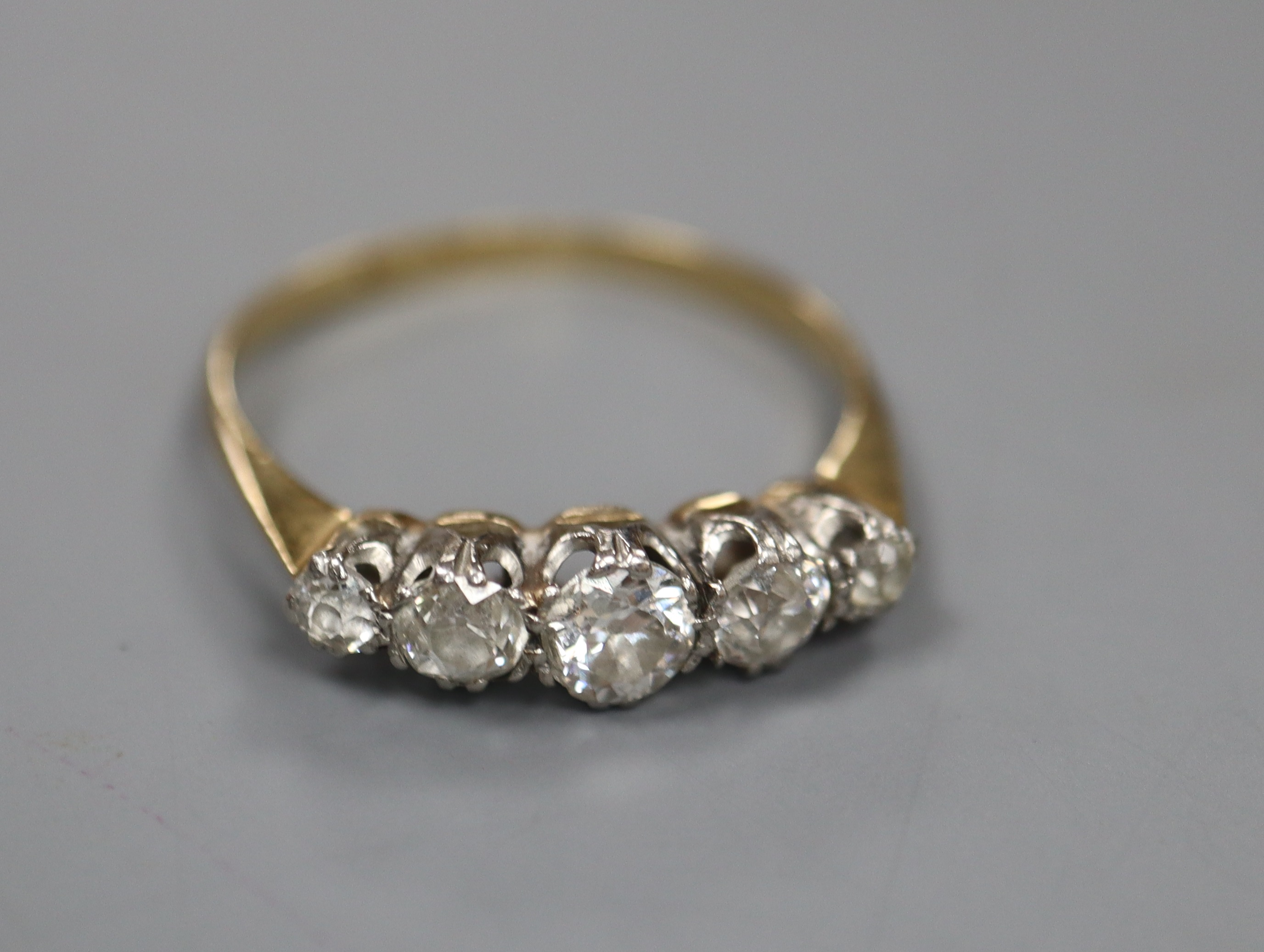 A yellow metal and graduated five stone diamond set half hoop ring, size O, gross 2.1 grams.